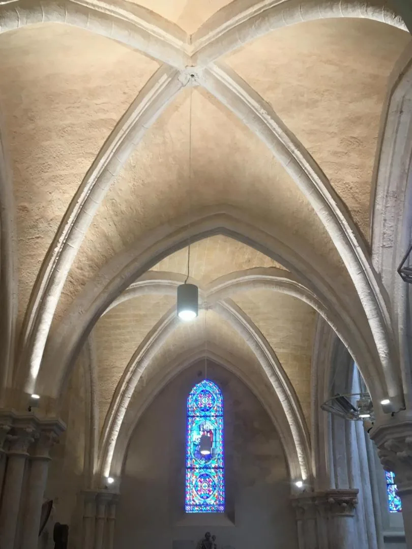 Voûtes gothiques d'une nef d'église éclairées par l'Entreprise Gilles, vitrail en arrière-plan